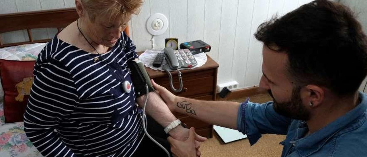 Jonathan González con su abuela, Dolores González, que muestra el medallón de teleasistencia, con un sensor en la esquina derecha, en la pared.