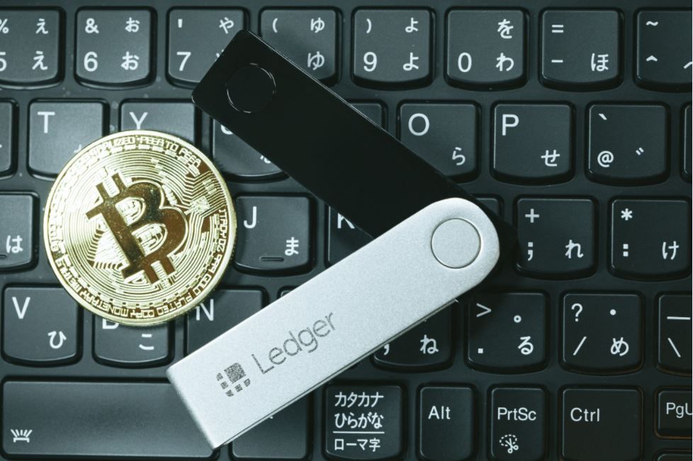 Una billetera de hardware sobre un teclado y una moneda simbolizando el Bitcoin