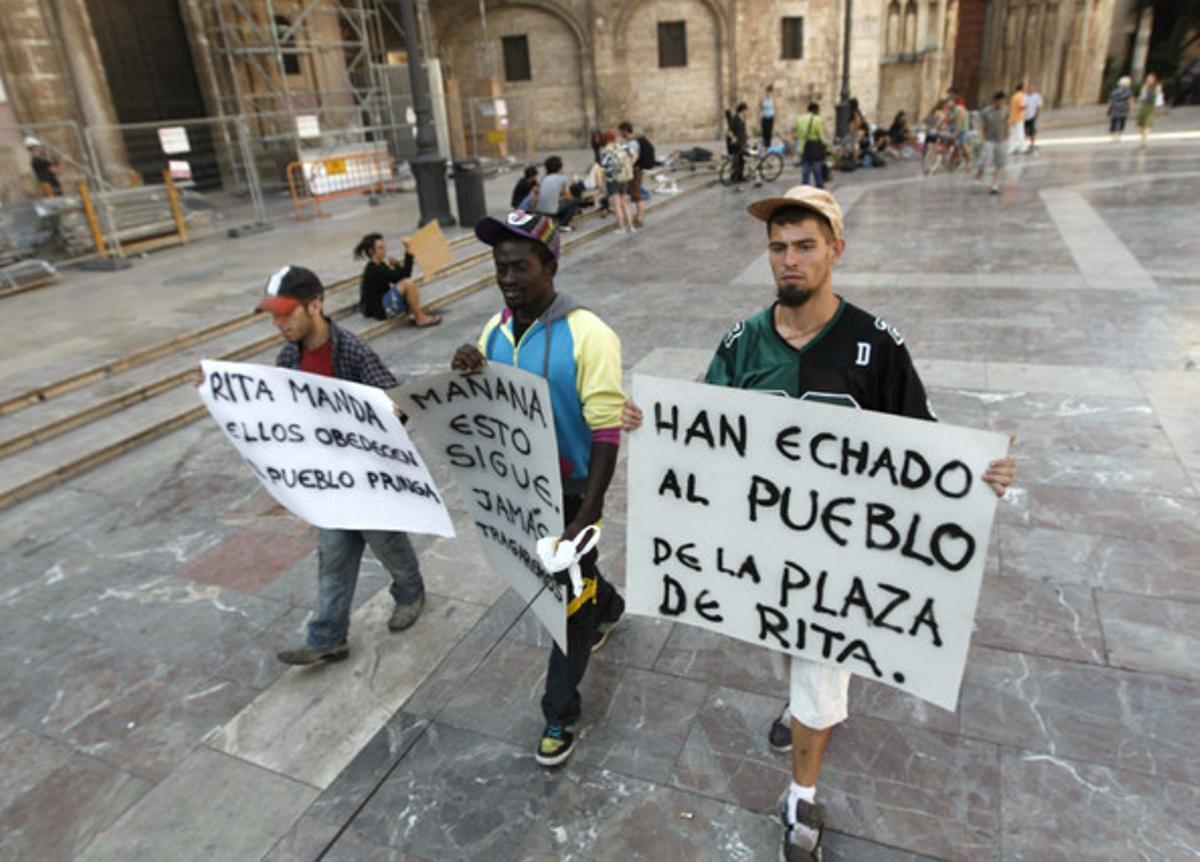 Tres participants en l’acampada de València es traslladen a la plaça de la Verge, després de ser desallotjats de la plaça de l’Ajuntament, aquest dimarts.