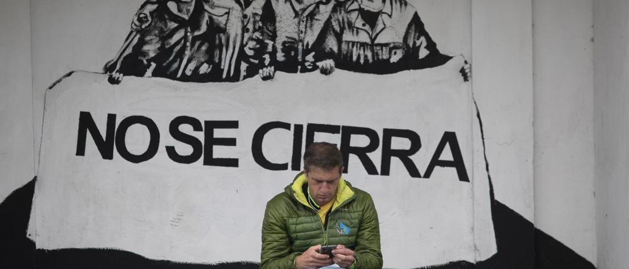 El presidente del comité de la fábrica de Alu Ibérica Avilés, José Manuel Gómez de la Uz, envía mensajes desde el teléfono móvil sentado en una marquesina próxima a la planta.