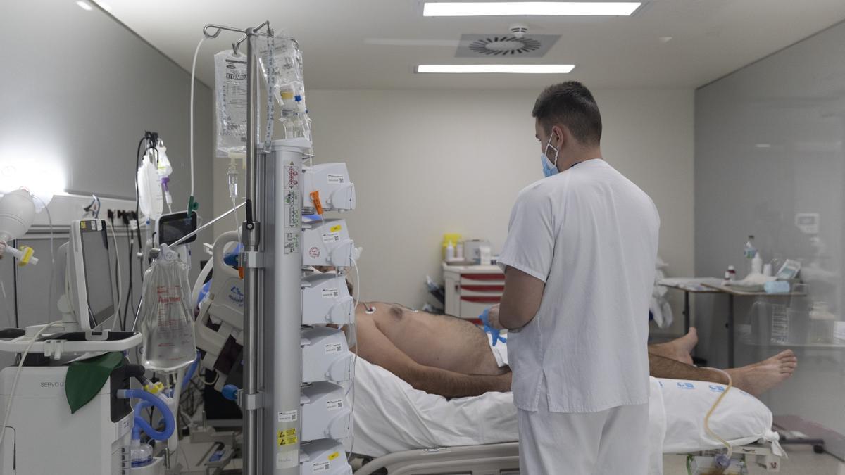 Un sanitario junto a un paciente ingresado en la UCI.