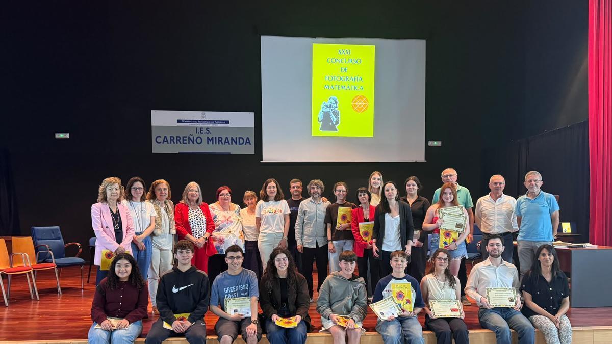 Foto de familia de los ganadores del concurso literario,  los premiados del concurso literario y de fotografía matemática con docentes de Lengua, Matemáticas y algunos profesores jubilados, en el salón de actos del IES Carreño Miranda, con el gaitero José Manuel Tejedor, en el centro.