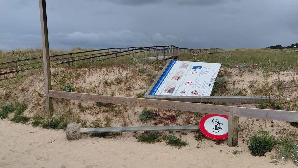 Uno de los carteles tirados y una señal en A Lanzada.
