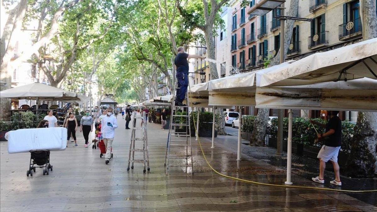 Unos trabajadores limpian los toldos de una terraza en La Rambla de Barcelona