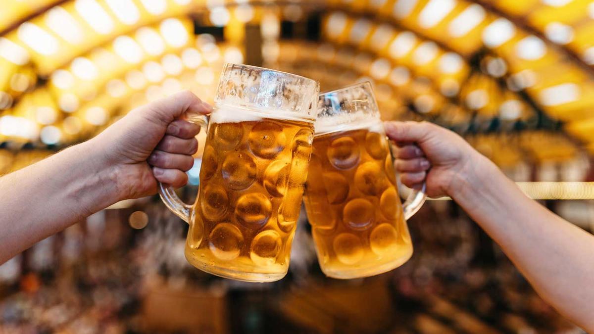 two hands clinking beer glasses in octoberfest marquee