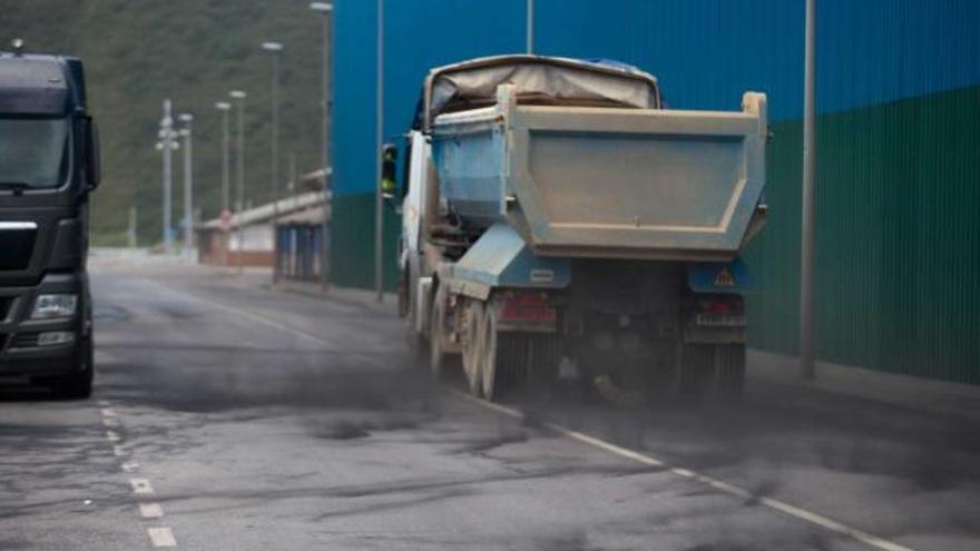 Un camión, circulando en dirección a la dársena de San Juan de Nieva levanta a su paso una nube de polvo de carbón; a la derecha, la pantalla metálica instalada para reducir el efecto contaminante de los minerales pulverulentos.