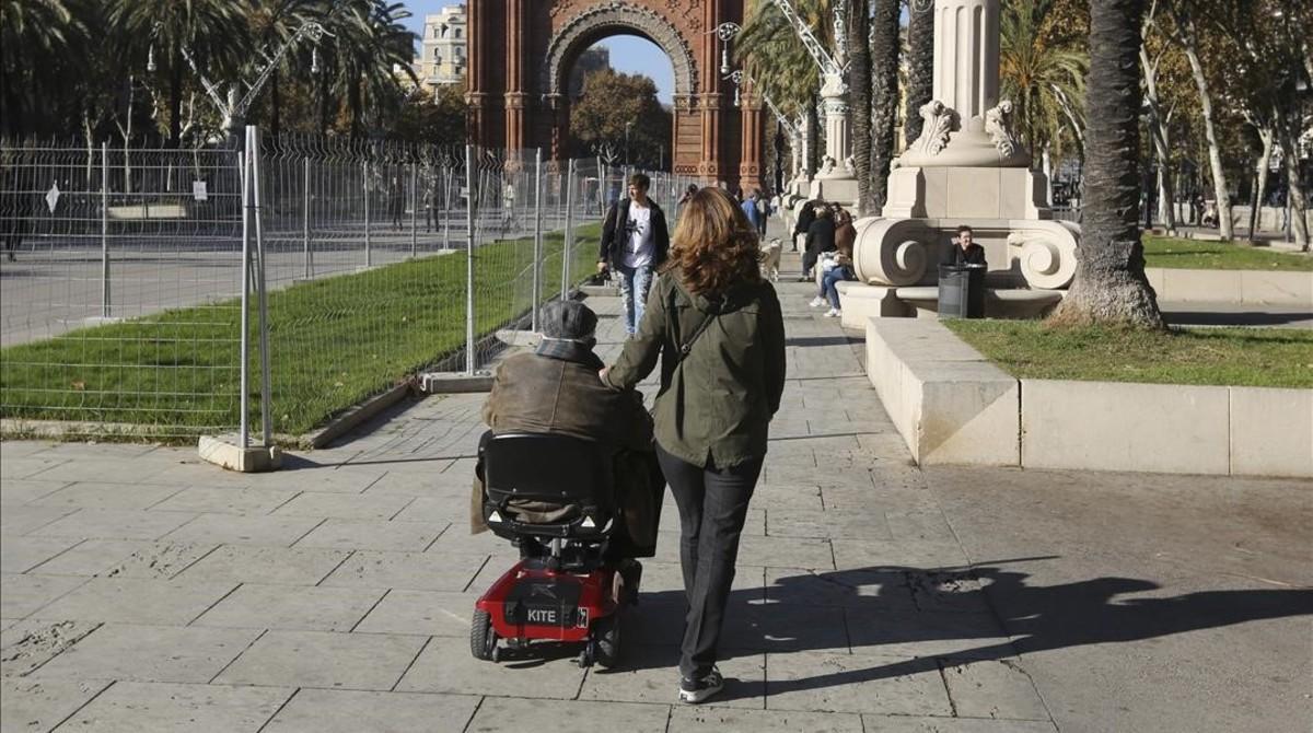 Una mujer pasea junto a una una persona dependiente por el entorno del Arc de Triomf de Barcelona.