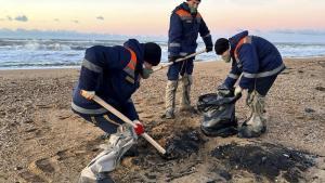 Tres trabajadores del Ministerio de Emergencias de Rusia retiran arena contaminada por el vertido de fuel de los dos petroleros naufragados en el mar Negro.