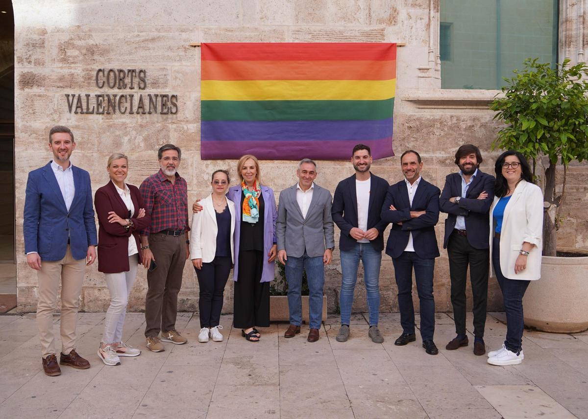 Representantes del PP y de la Conselleria de Igualdad posan tras colgar la bandera LGTBI en las Corts.
