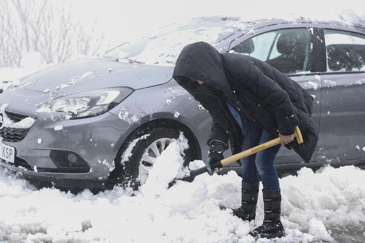 Una mujer trata de despejar la nieve acumulada para poder circular con el vehículo este sábado en O Cebreiro