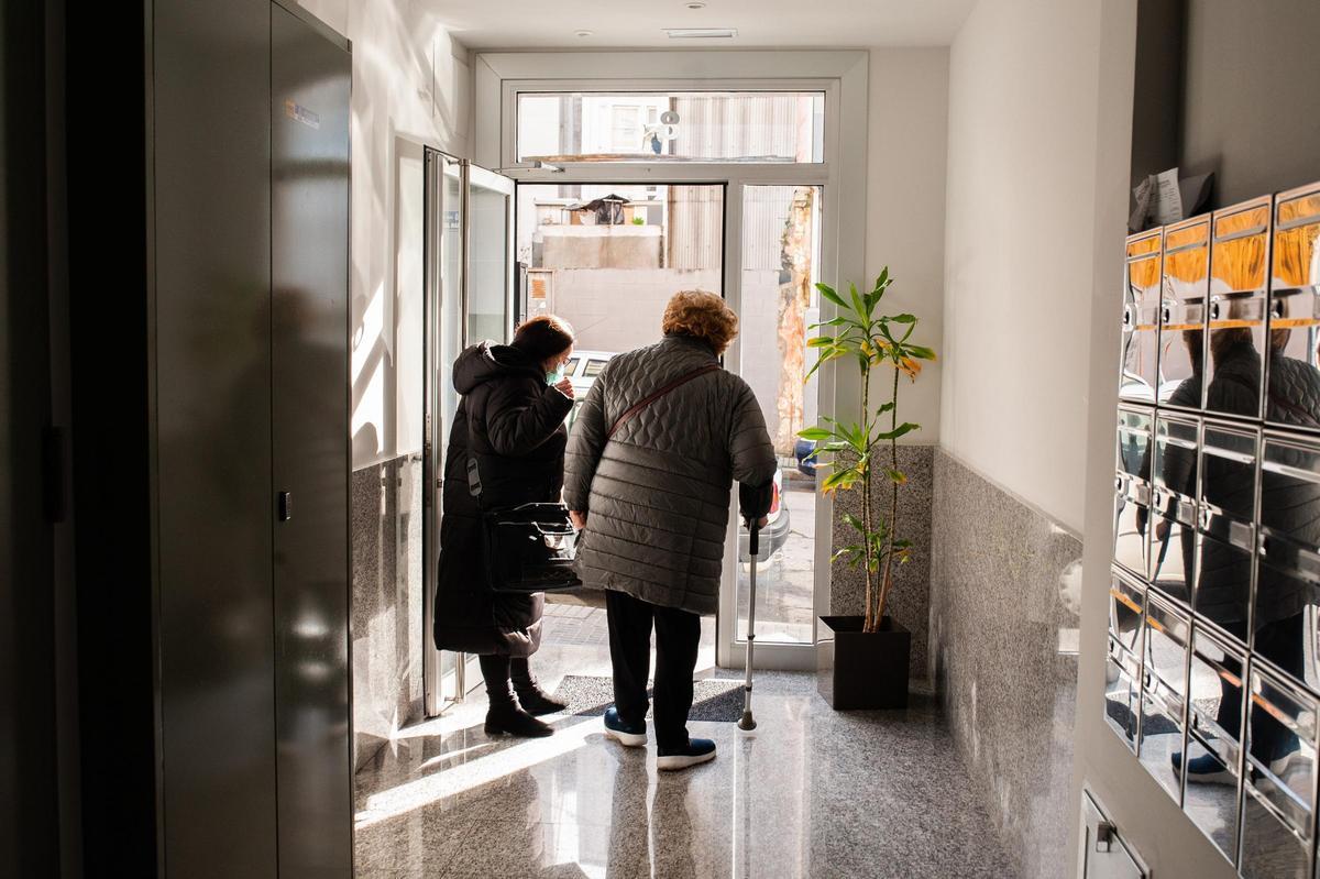 Una trabajadora de ayuda en el hogar con una usuaria en el portal de un domicilio.