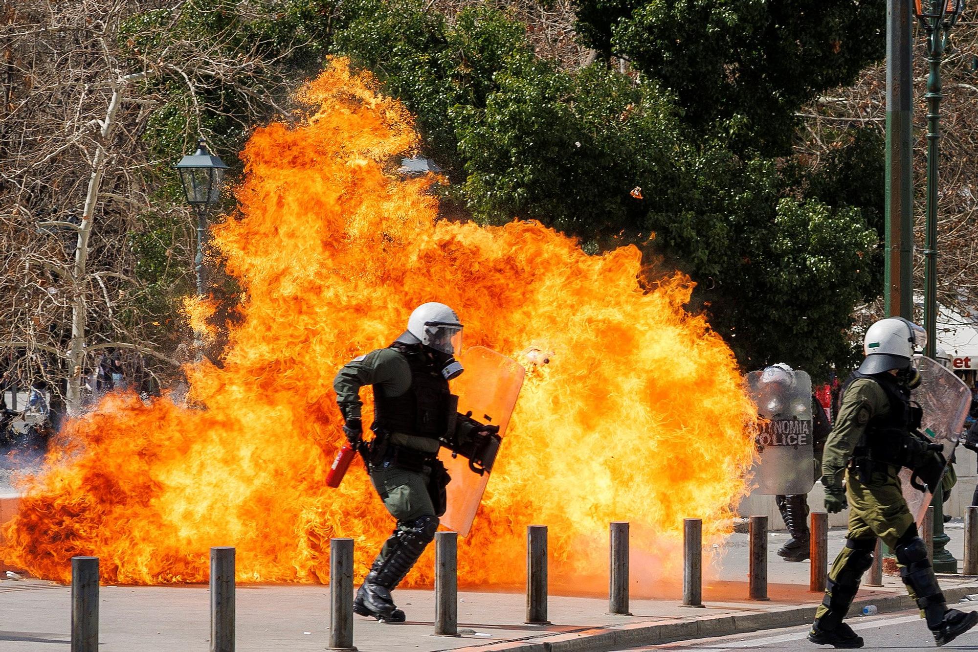 Policías antidisturbios pasan frente a un fuego durante los choques con manifestantes en el centro de Atenas, este domingo.