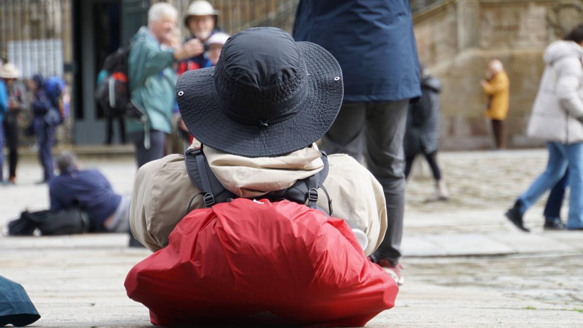 Un peregrino descansa en el Obradoiro mientras observa la fachada de la Catedral