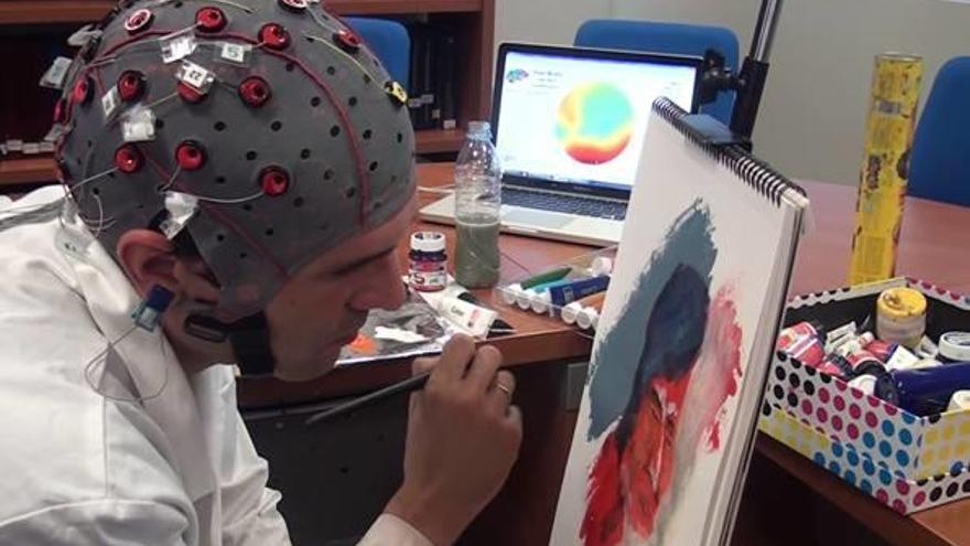 Un artista pintando un lienzo con un casco con vectores para analizar el comportamiento de su cerebro mientras crea una obra de arte.