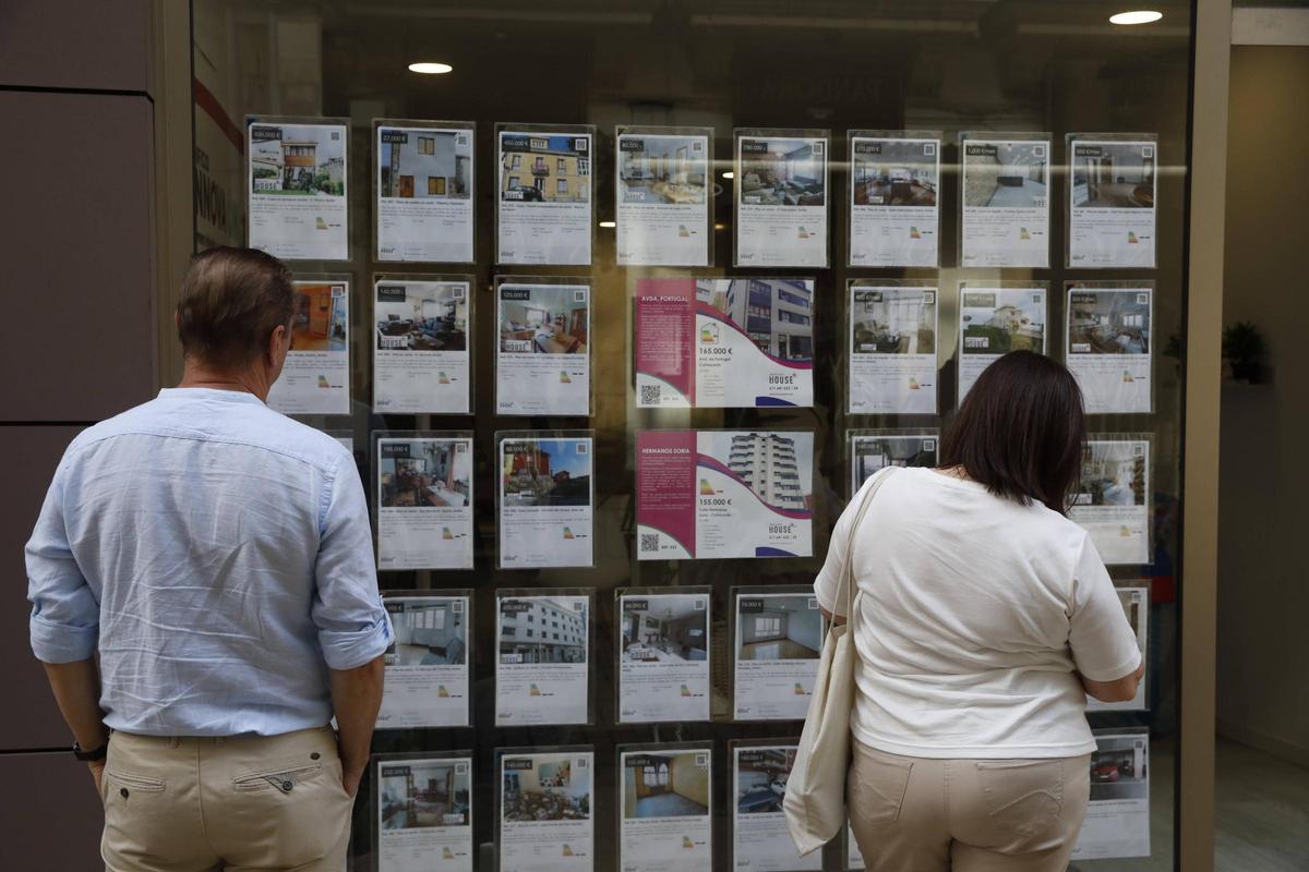 Dos transeúntes contemplan ofertas inmobiliarias en una agencia de Avilés.
