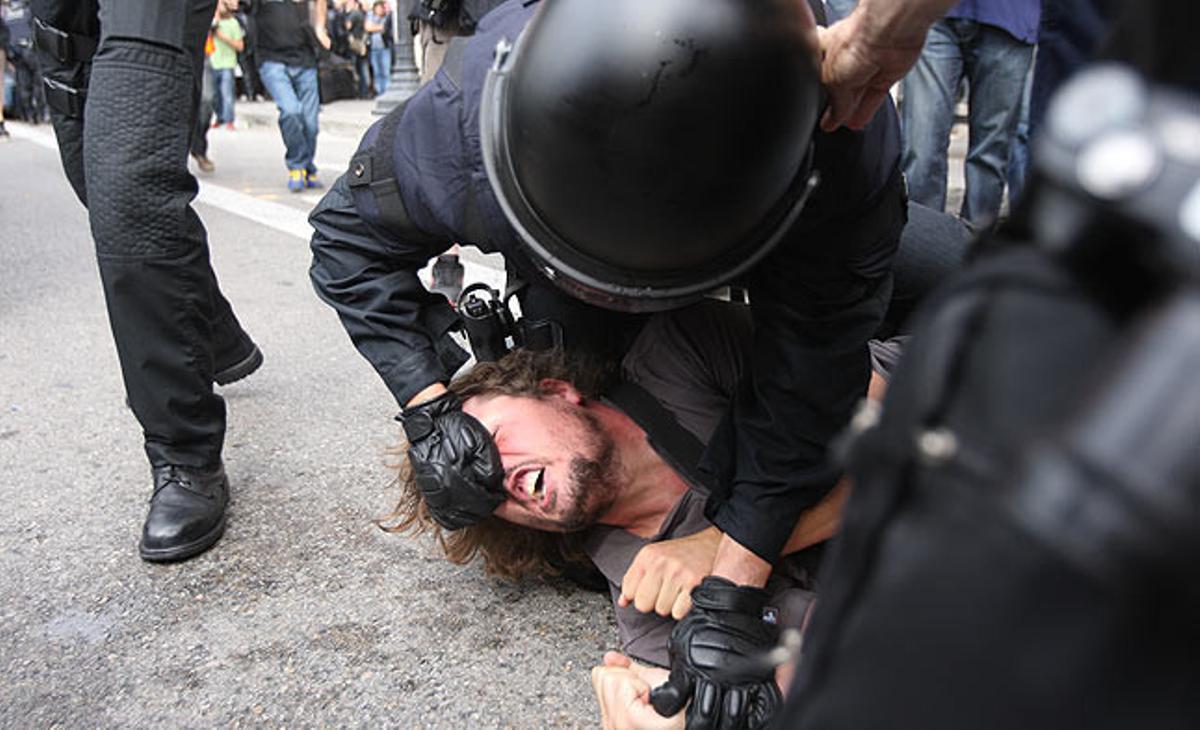 Agents antiavalots immobilitzen un dels acampats de la plaça de Catalunya, aquest divendres.