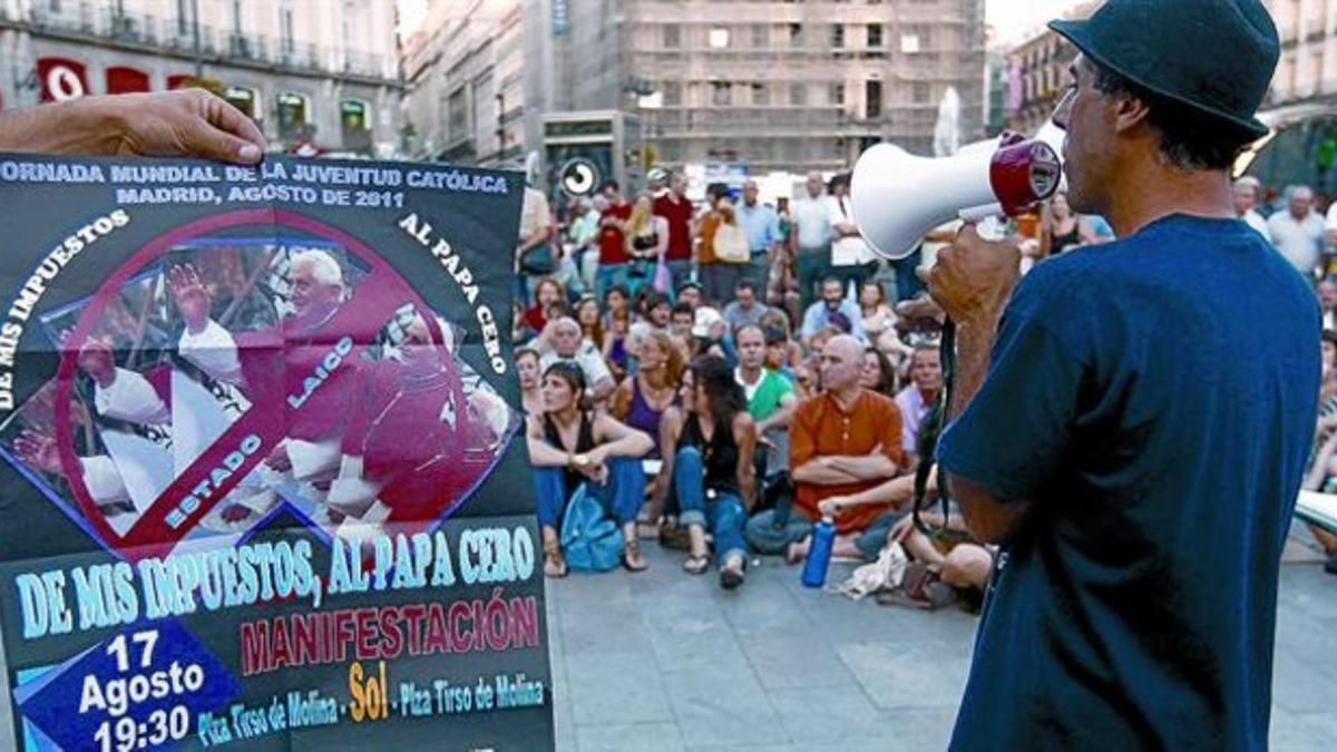 Un cartel crítico con la visita del Papa presidía ayer una asamblea de indignados celebrada en la Puerta del Sol.