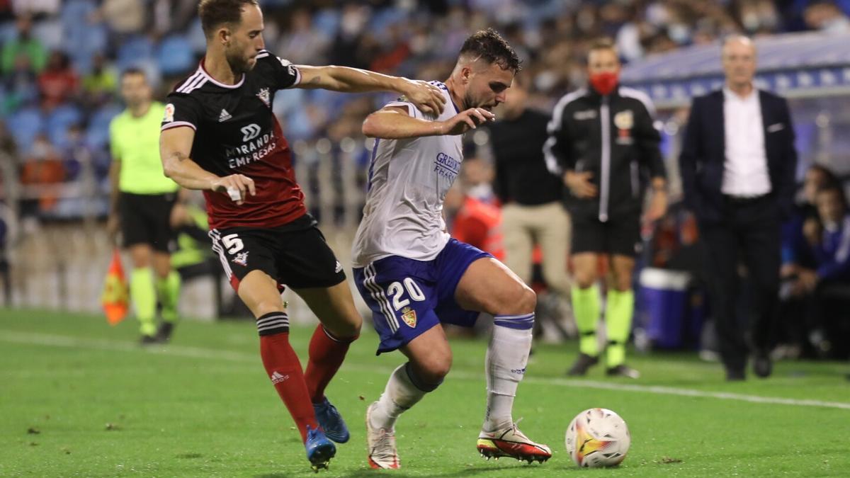 Álvaro Giménez protege el balón, con JIM, difuminado, al fondo.