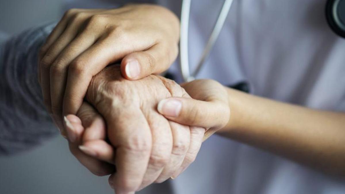 Una enfermera sostiene la mano de un anciano.
