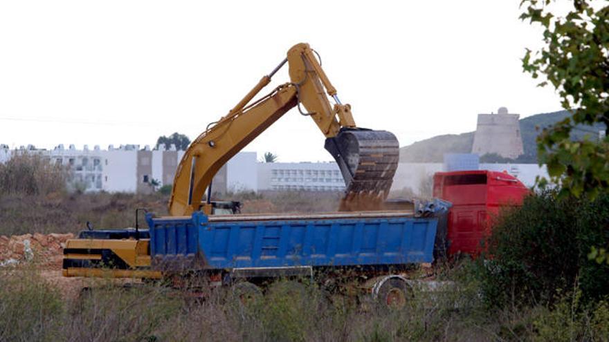 Una excavadora carga tierra en un camión, con la vista de la torre de sa Sal Rossa al fondo.