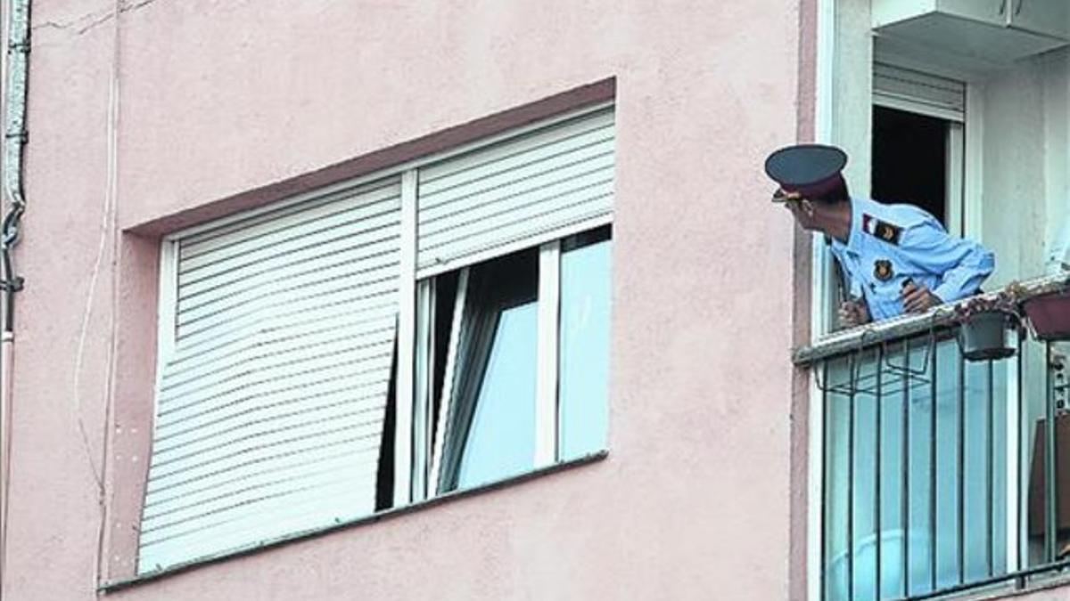 Un mosso inspecciona desde el balcón la vivienda afectada.