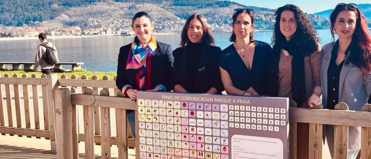 Fotografia del mural con el comunicador Praia y las logopedas que lo realizaron. Va El Faro de Vigo