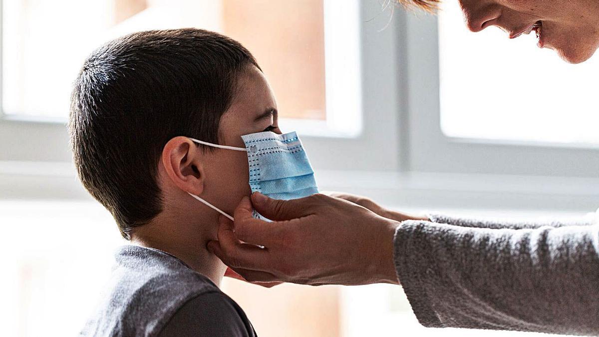 Una mujer coloca una mascarilla higiénica a un niño. |   // IÑAKI BERASALUCE