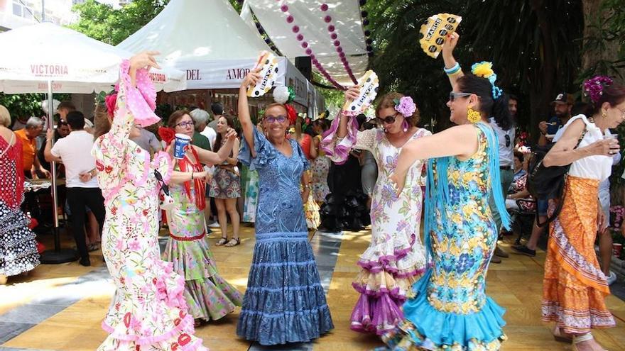 Un grupo de mujeres vestidas de flamenca bailan al son de las sevillanas en la portada de la feria de día, ubicada en el Parque de la Alameda