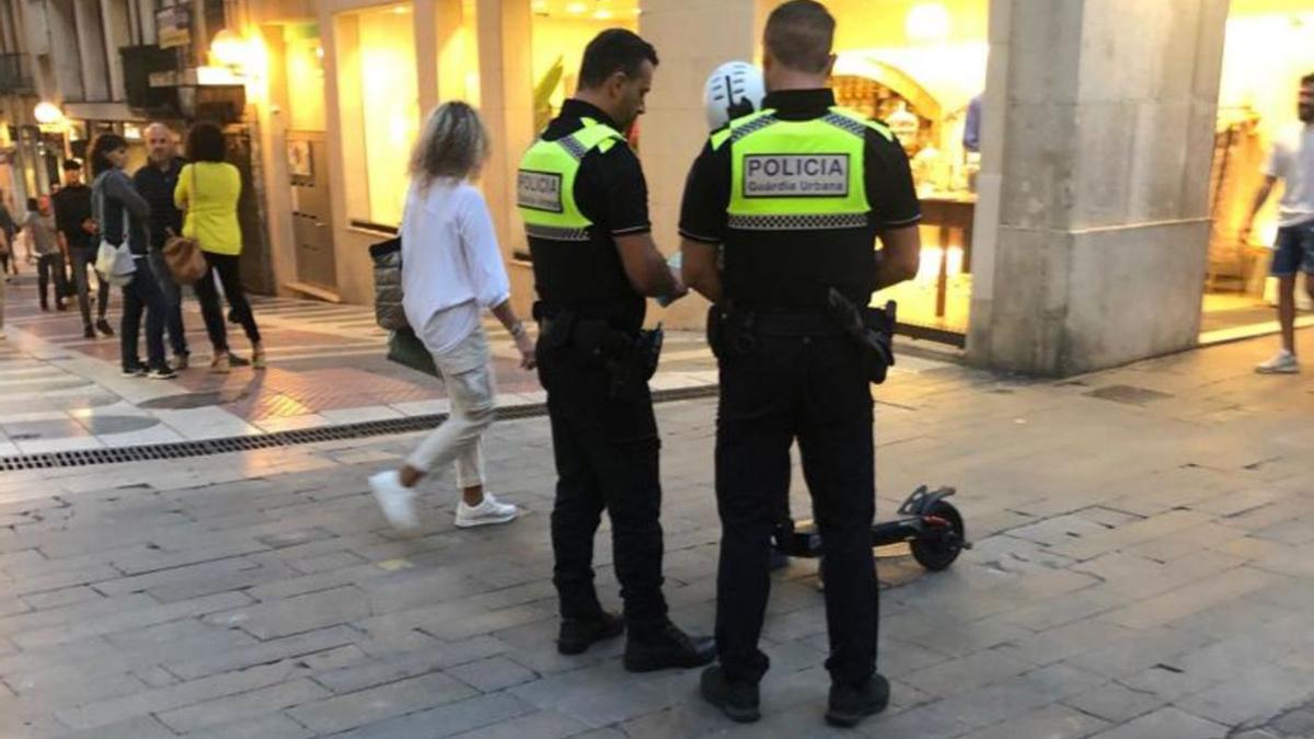 Dos agents de la Guàrdia Urbana amb l’usuari d’un patinet a la plaça de l’Ajuntament.