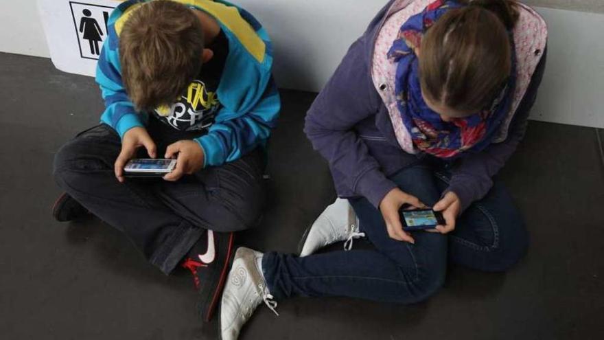 Dos niños miran las pantallas de sus teléfonos móviles.