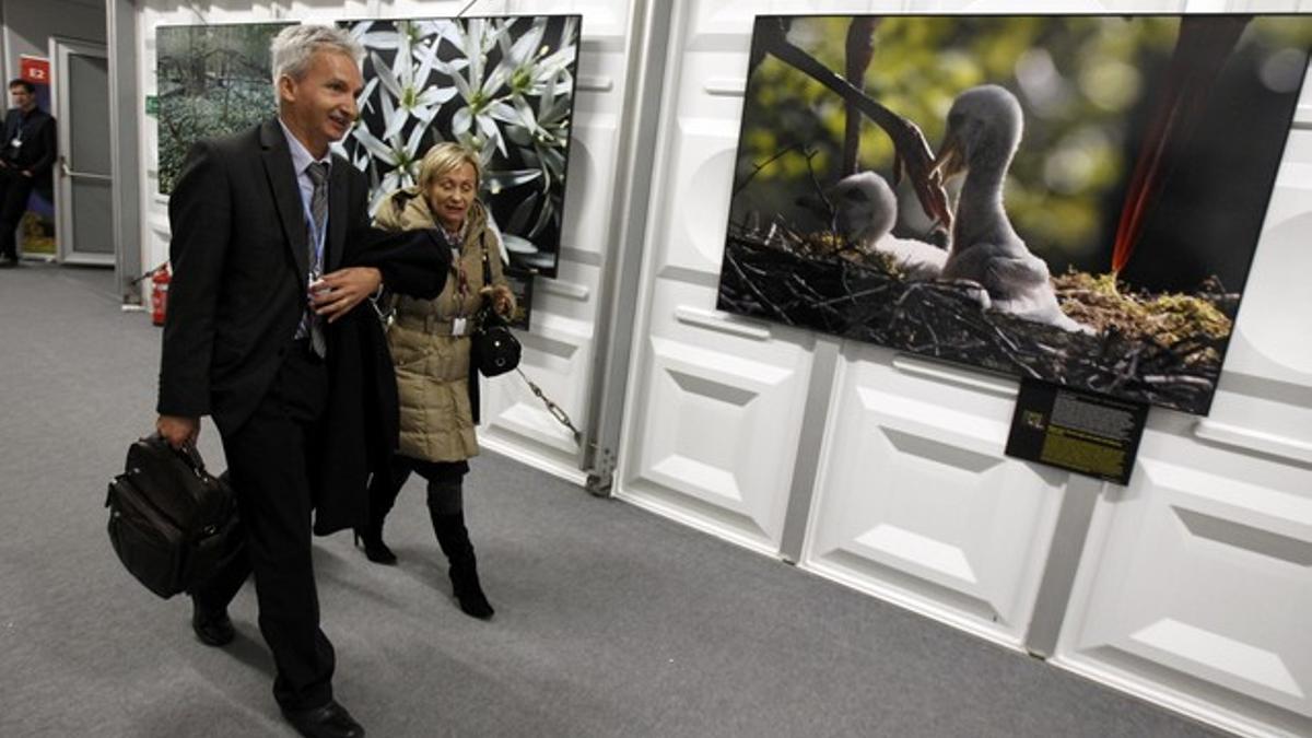 Dos delegados en la cumbre sobre el cambio climático caminan ante una exposición de fotografías en el Estadio Nacional de Varsovia.