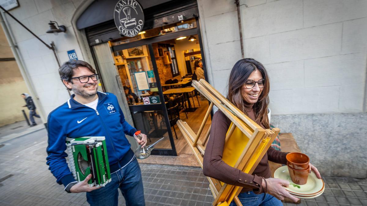 Dos clientes de L'Antic Colmado salen del restaurante con algunas de las piezas de segunda mano para llevar: platos, vasos, porrón, una máquina de escribir Olympia y hasta una silla plegable.