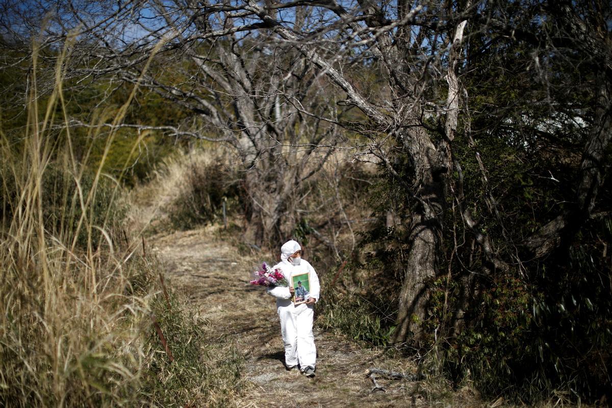 Hisae Unuma usa un traje de protección mientras se dirige al cementerio de su familia cerca de la casa en la que vivía antes de ser evacuada, que está a 2,5 km de la dañada planta de energía nuclear de Fukushima,  en el aniversario de la muerte de su esposo