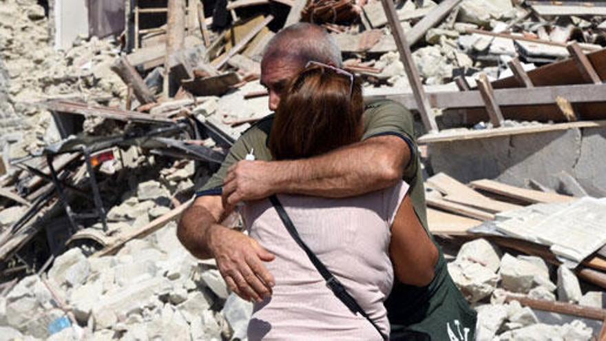 Dos lugareños se abrazan frente a su casa derruida.