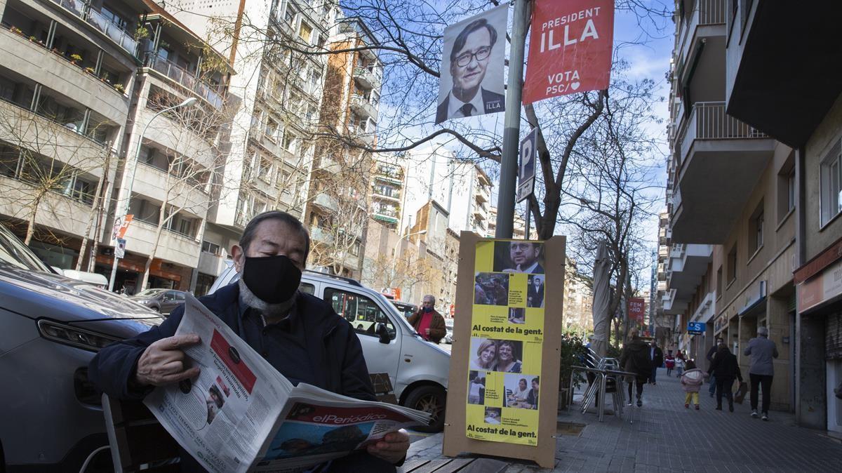 Un lector de EL PERIÓDICO siguiendo la información junto a los carteles  electorales del PSC y ERC.