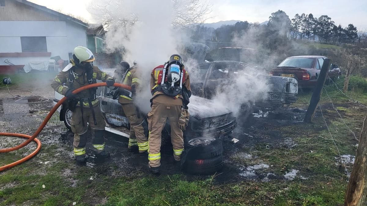 Los bomberos sofocando las llamas de los dos coches calcinados.