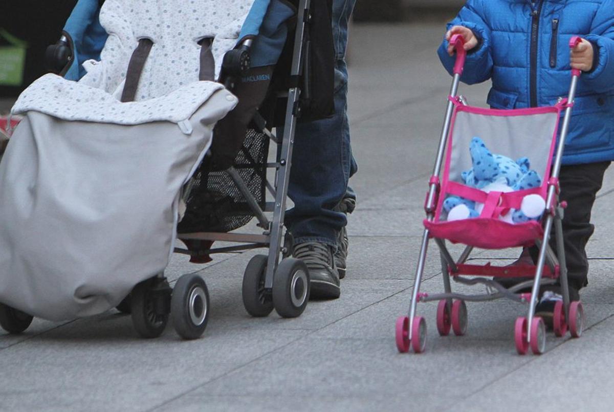 Un adulto porta una silla de bebé y un niño lleva al lado una de juguete. | IÑAKI OSORIO