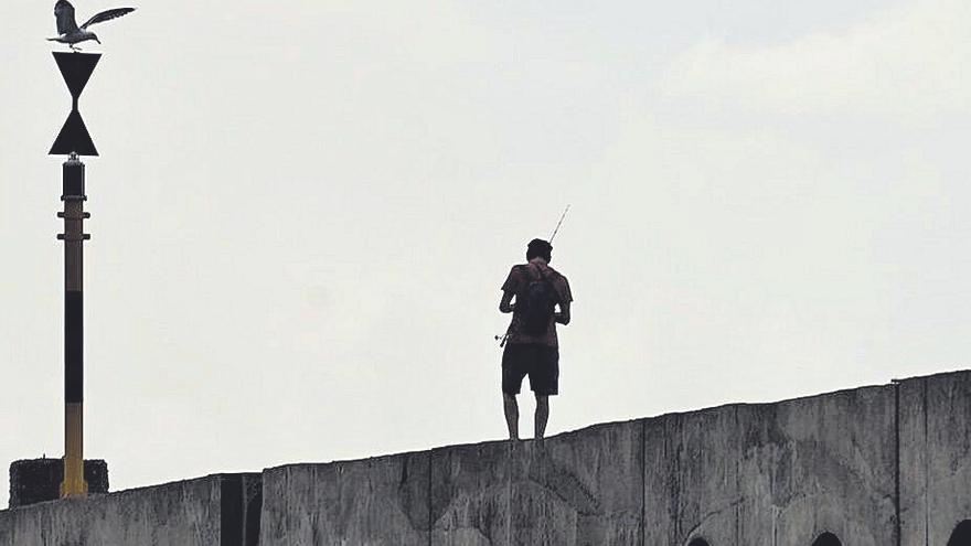 Un pescador sobre el muro del dique de la playa bagañete.