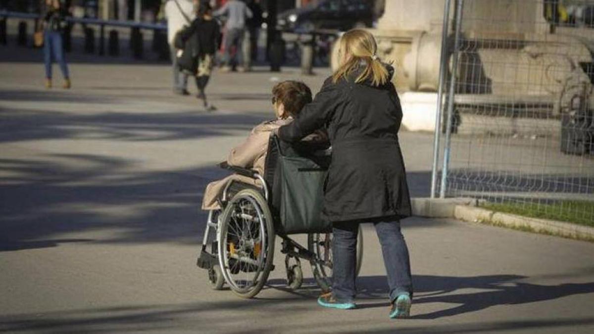 Una persona ayuda a una persona dependiente en silla de ruedas.