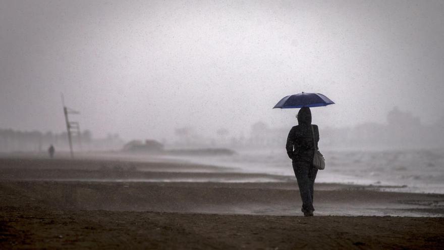 Una persona pasea por la playa bajo la lluvia.