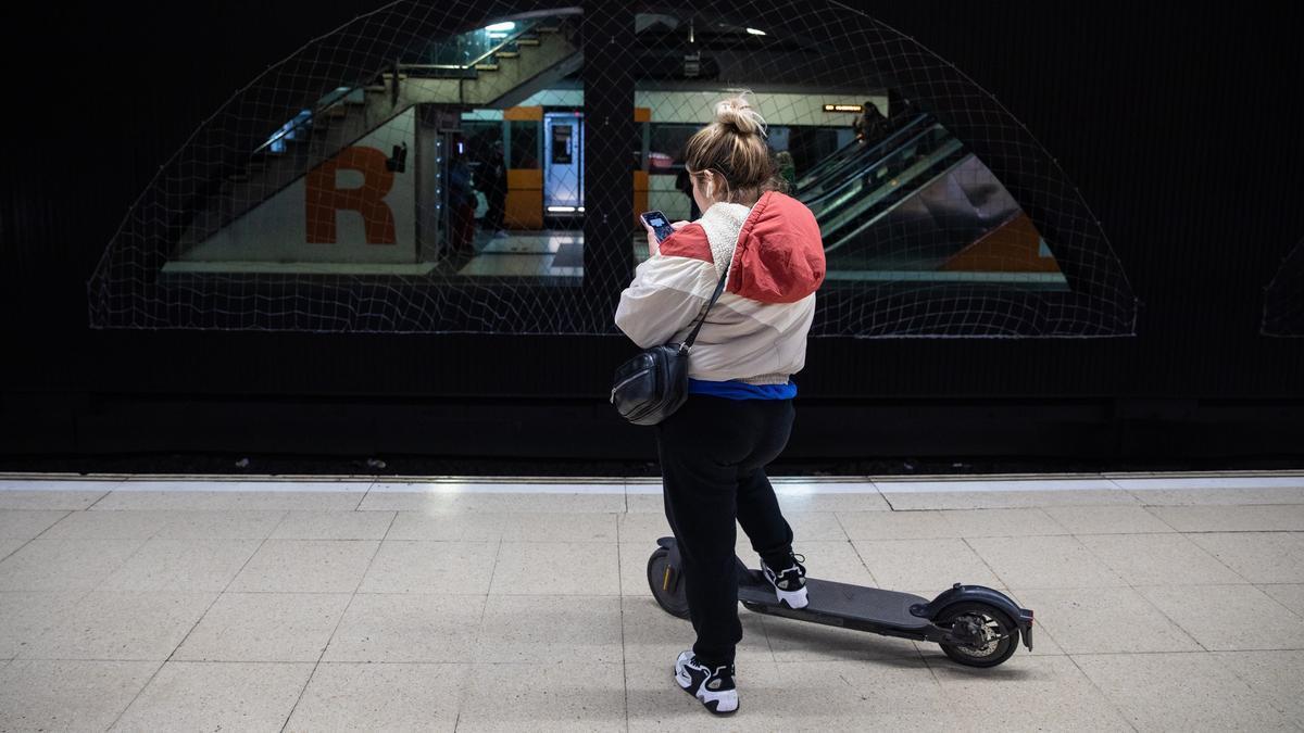 Una dona amb un patinet elèctric esperant en una estació de Renfe