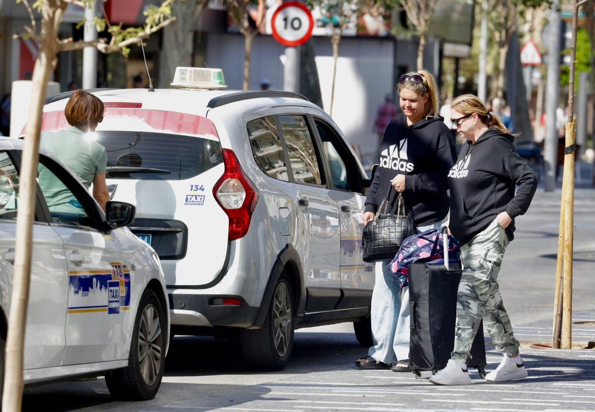 Dos mujeres cargadas con una maleta se suben a un taxi de Benidorm, este jueves.