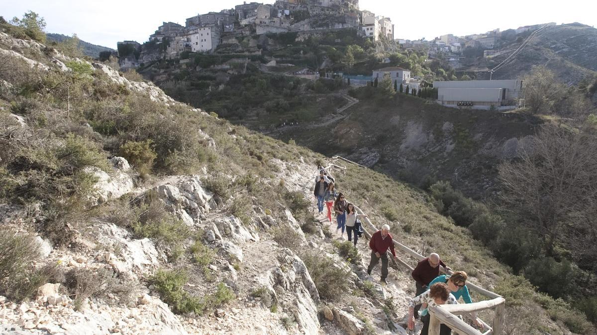 Un grupo de turistas accede a la ruta de les Covetes de Bocairent, con el Barri Medieval y los huertos al fondo.