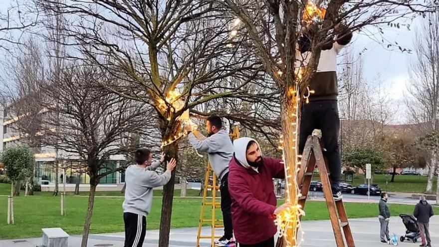 Miembros de la comisión de fiestas, ayer instalando los adornos en árboles de la plaza de Santa Cruz.   | // L.O.