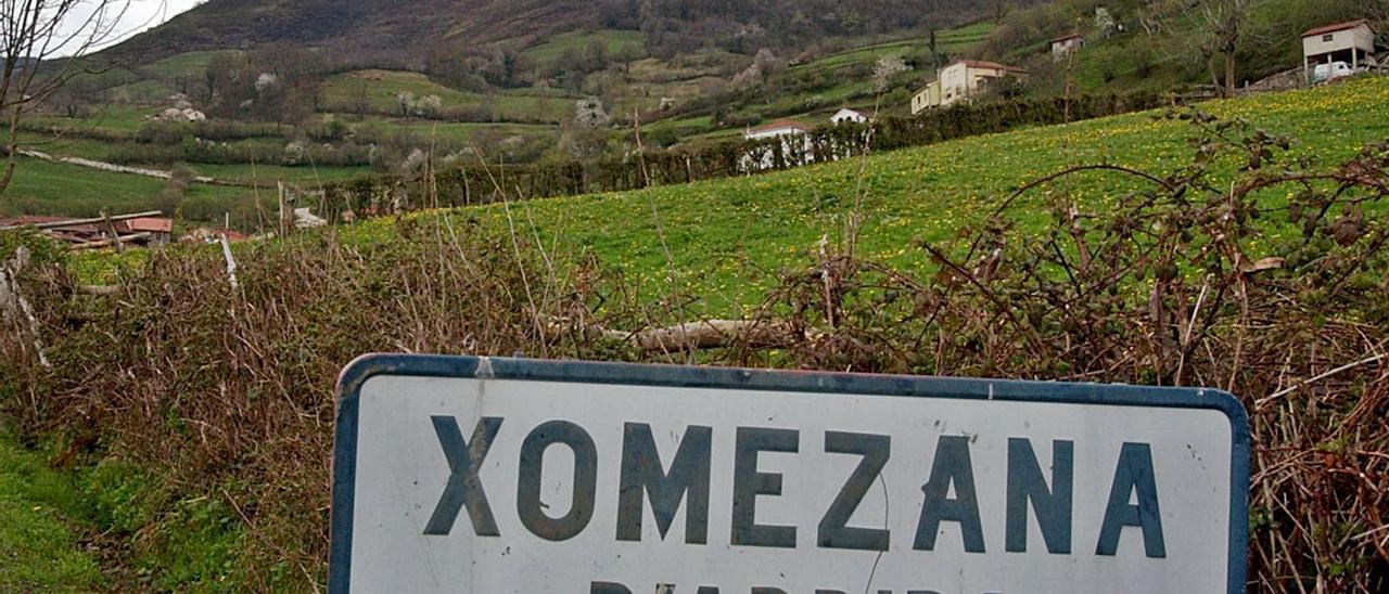 Cartel de entrada al pueblo de Xomezana de Arriba, con el pueblo al fondo.