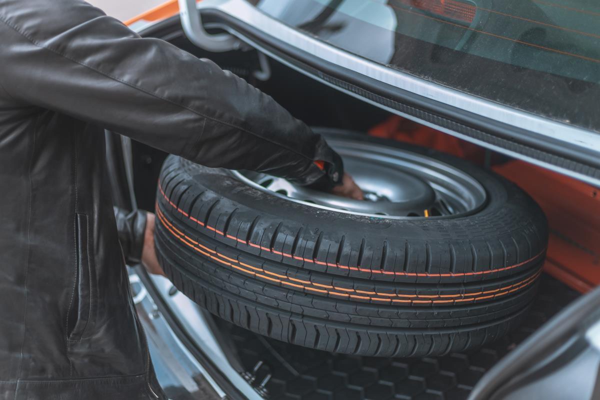 Un operario saca una rueda de recambio del maletero de un coche.