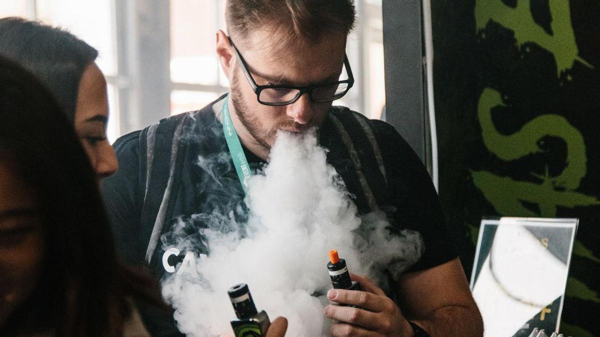 Una pareja expulsa vapor por la boca tras aspirarlo de sus vapeadores.