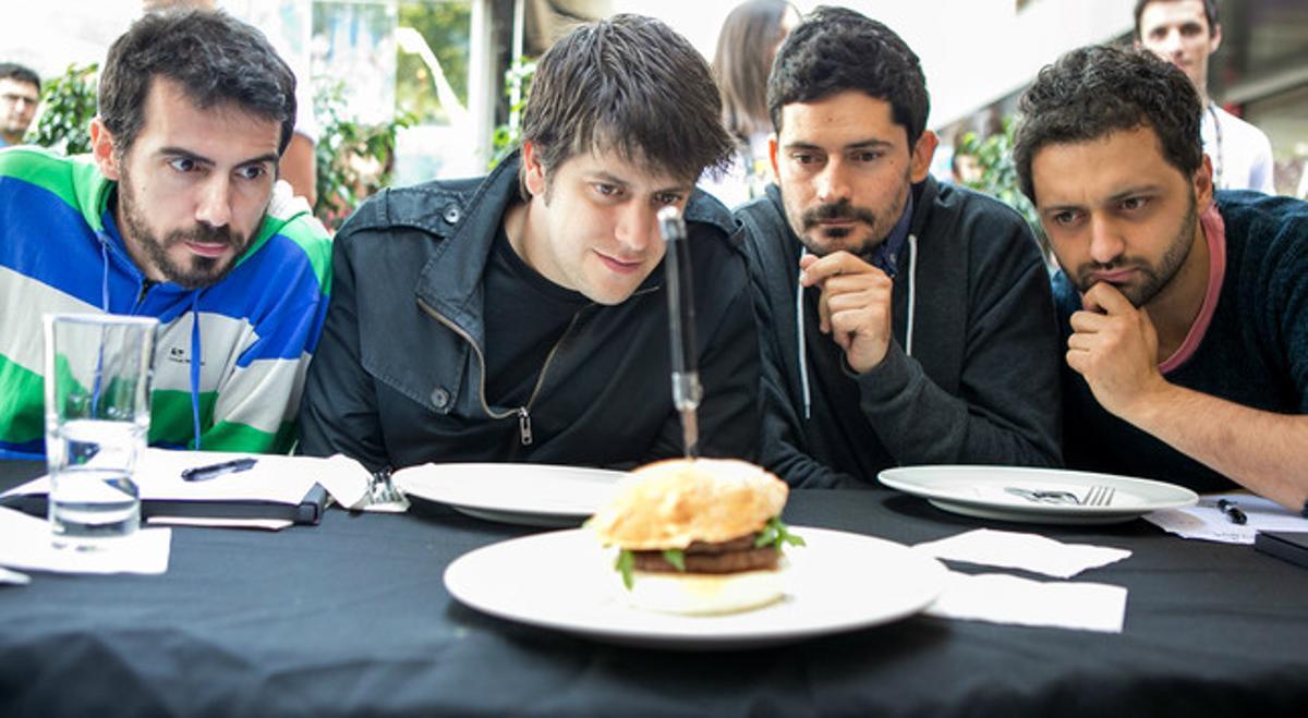 Els quatre integrants de la banda Els Amics de les Arts observen l’hamburguesa que porta el seu nom. 