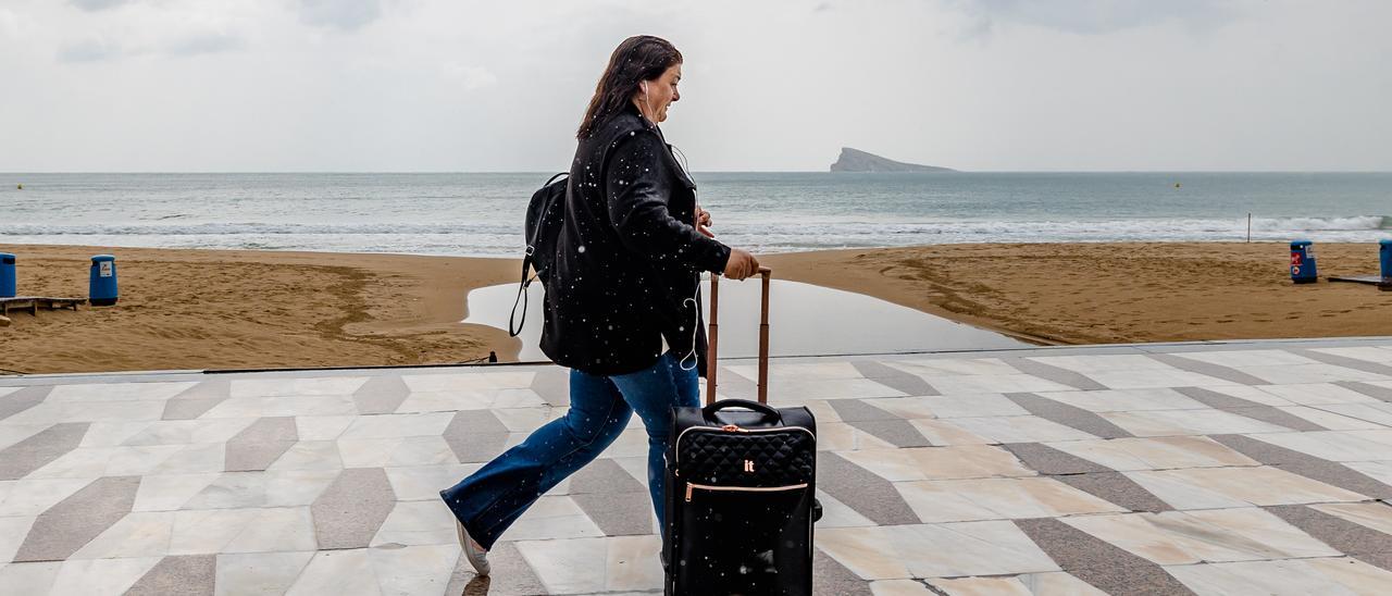 Una turista pasea por la primera línea de la playa de Levante con su maleta bajo la lluvia, que según las previsiones desaparecerá a partir del jueves.