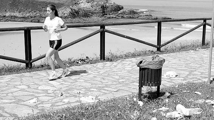 Una mujer corriendo, ayer, por el paseo de la playa tapiega, con basura esparcida.
